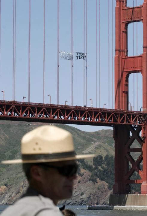 A Golden Gate National Park ranger keeps spectators away from the water as three demonstrators scale the south tower of the Golden Gate Bridge and unfurl a banner intended to draw attention to Chinese human rights violations in Tibet in San Francisco, California, on April 7, 2008. Protestors are staging demonstrations against the Chinese government as the city of San Francisco prepares to host the Olympic torch relay on Wednesday. San Francisco is on tenterhooks ahead of the Olympic flame's procession through the city on April 9, which follows London and Paris events which were severely disrupted by pro-Tibet protesters. AFP PHOTO/ Ryan Anson (Photo credit should read Ryan Anson/AFP/Getty Images)