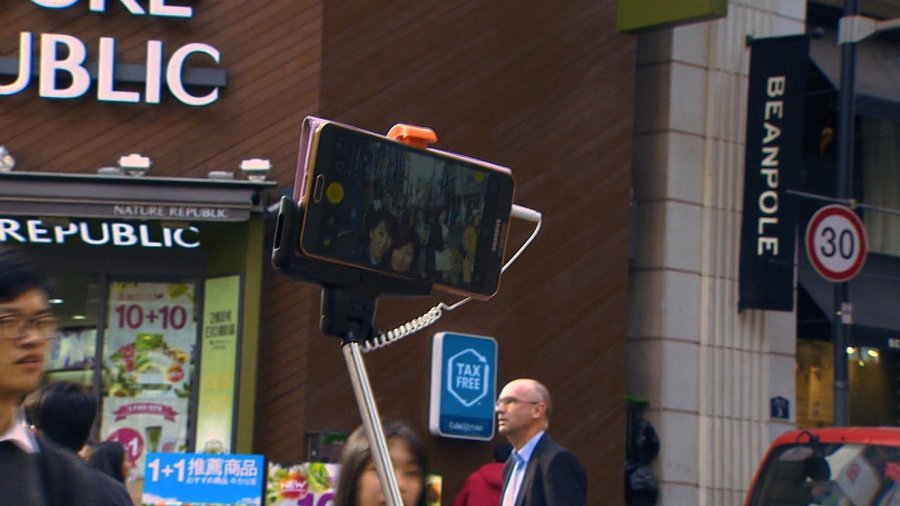 A couple in Hong Kong uses a selfie stick, a long pole used to extend their camera phone more than three feet away allowing a wide frame for the photograph.