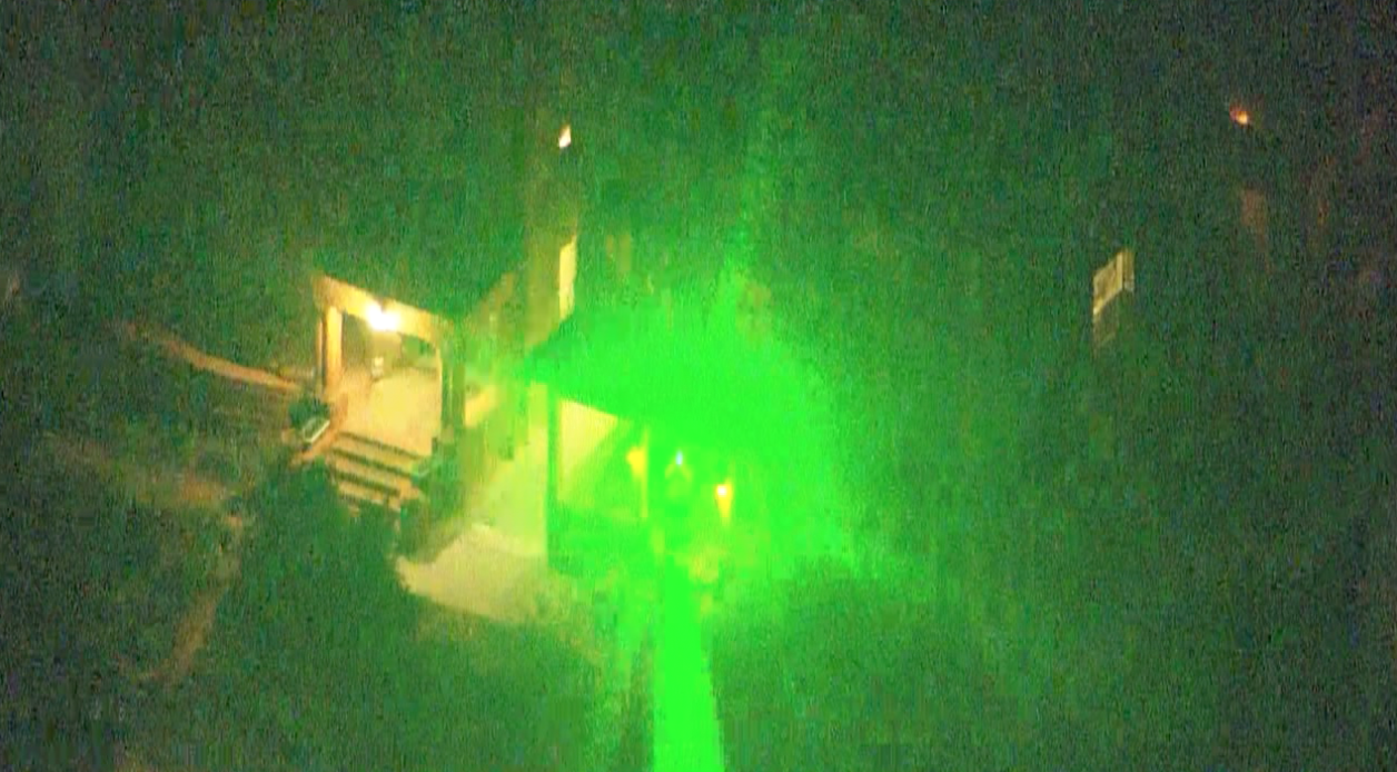 A green laser shines from a building toward the camera lens