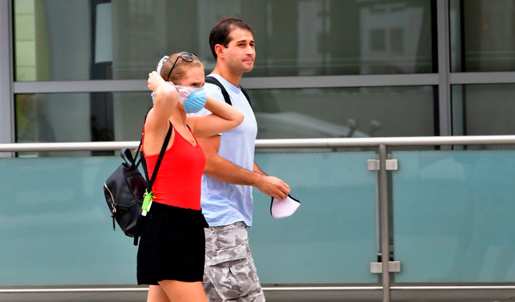 A woman adjusts her facemask as a man holds onto his while walking in Los Angeles on June 29, 2020. (Photo by FREDERIC J. BROWN/AFP via Getty Images)