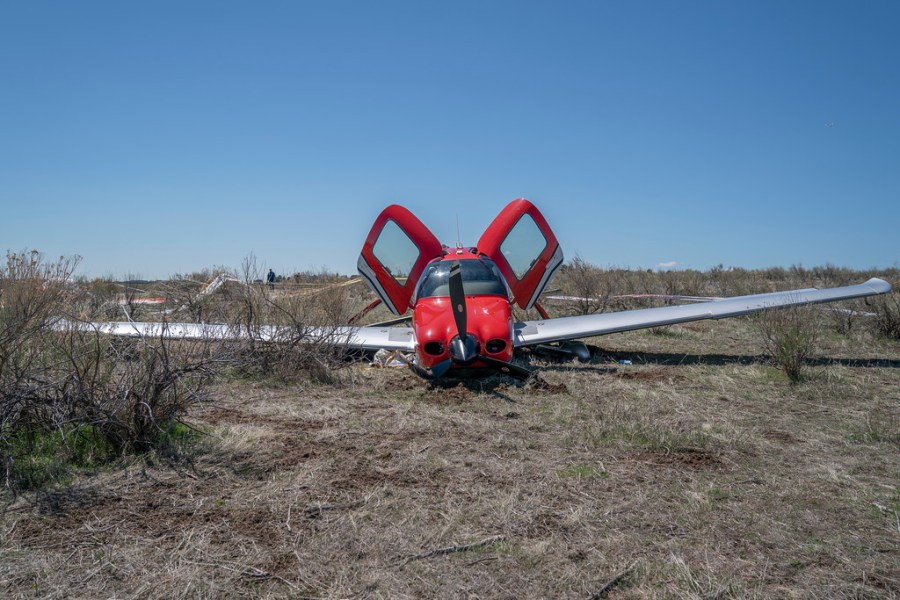 A small red and white airplane on dry dirt with its two doors lifted open on a field of dry dirt with blue sky