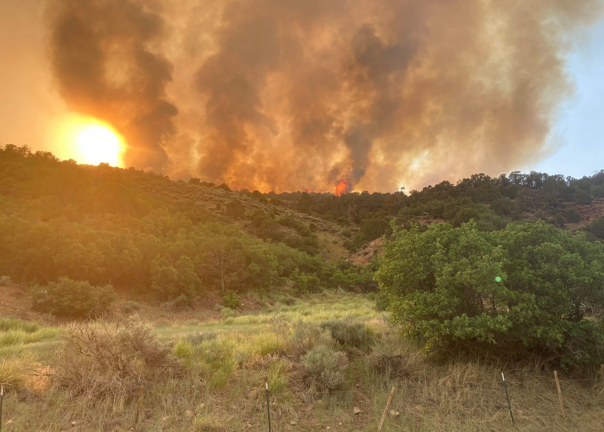 Fire burning behind the hills at dusk with dark smoke billowing