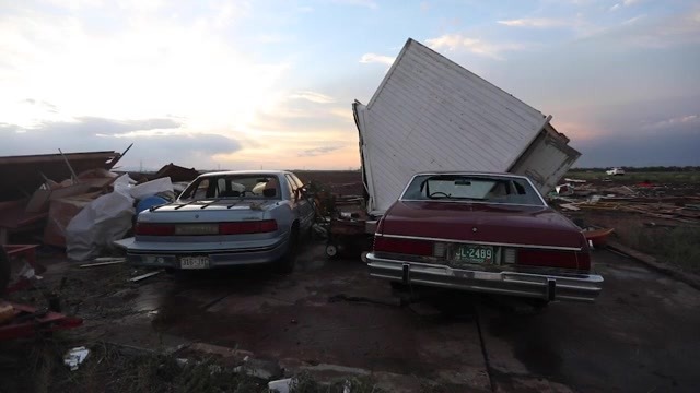 A shed on top of a car in the evening with another damaged car next to it