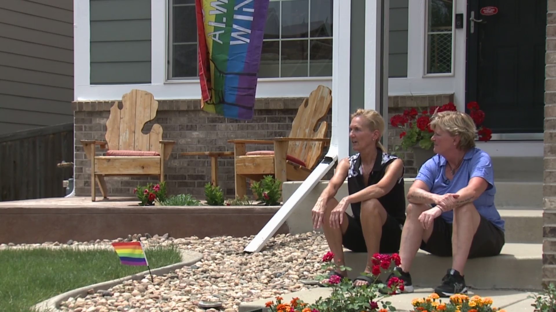 2 women sitting in front of their home with a rainbow flag nearby