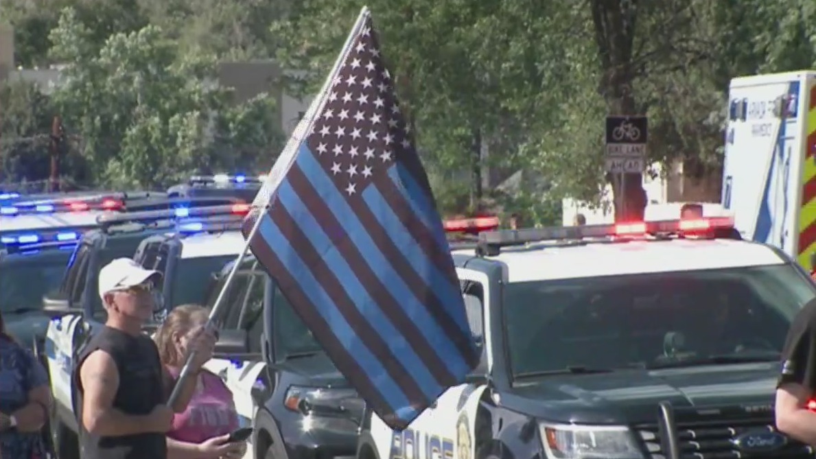 A man stands beside police vehicles with an American flag with the stripes colored blue and black