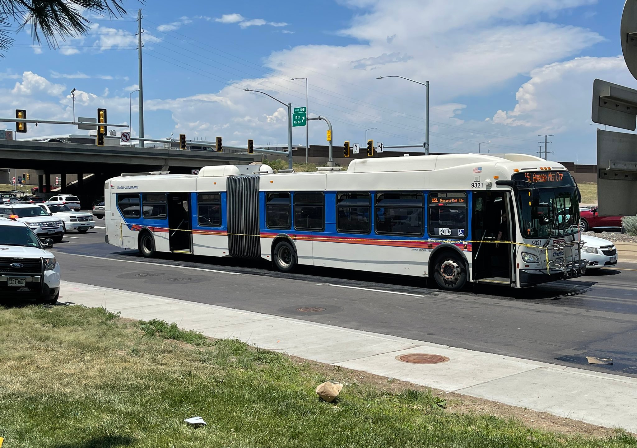 A city bus wrapped in crime scene tape on the street, just beside an interstate overpass, with police vehicles around it