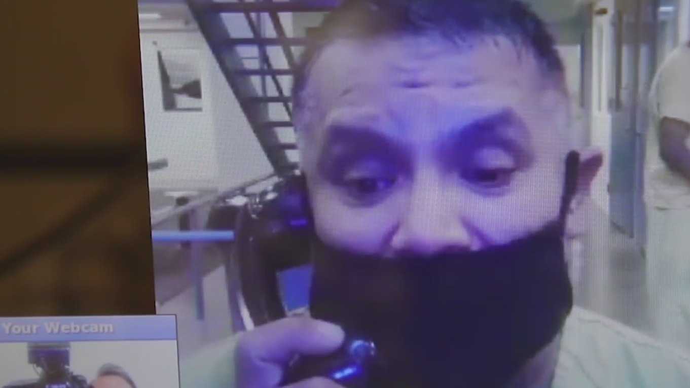 A man speaks on a telephone with a face mask with jail interior in background