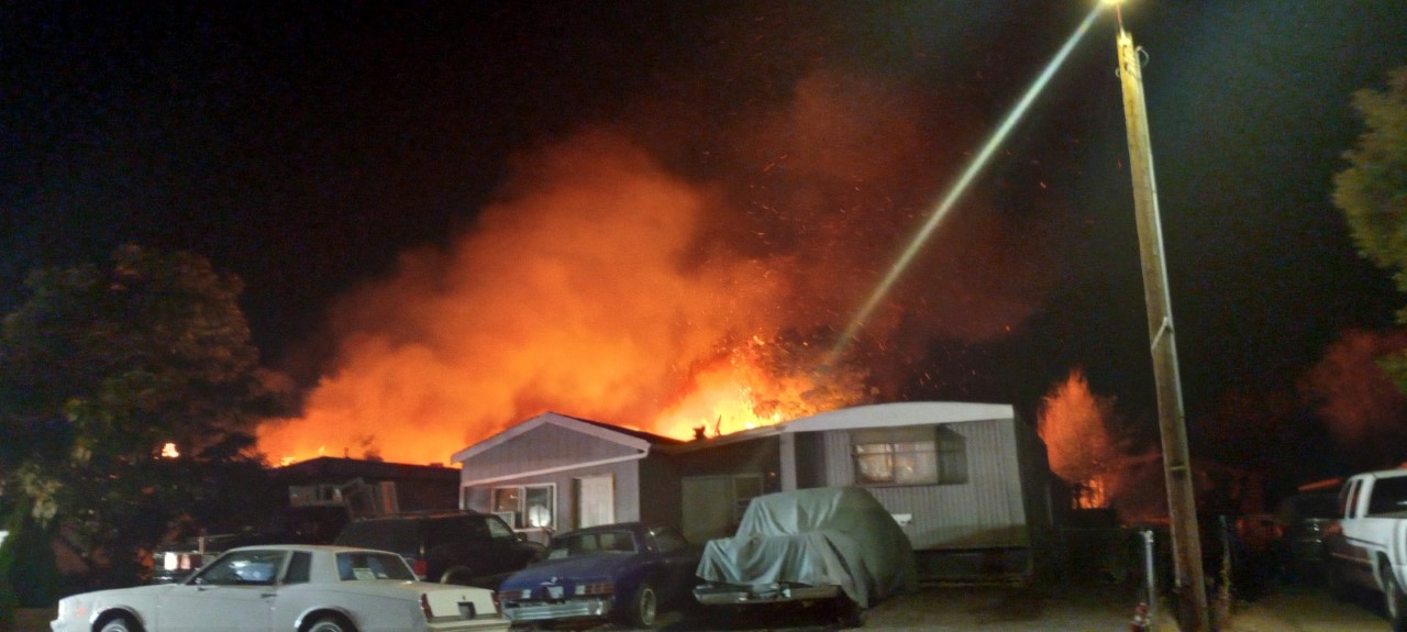 A mobile home at night with bright orange flames and smoke billowing from the roof