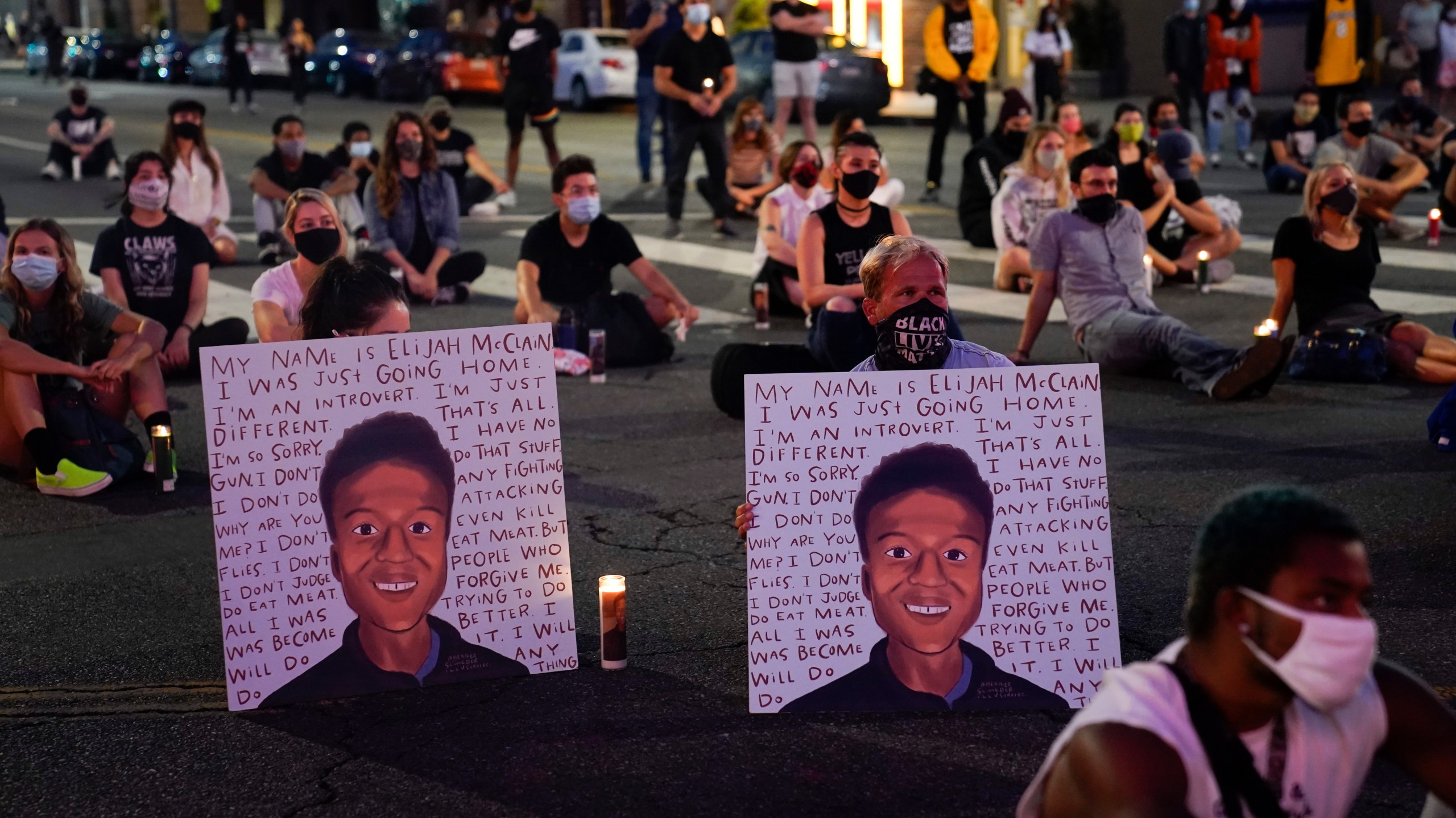 two people hold posters showing images depicting Elijah McClain during a candlelight vigil