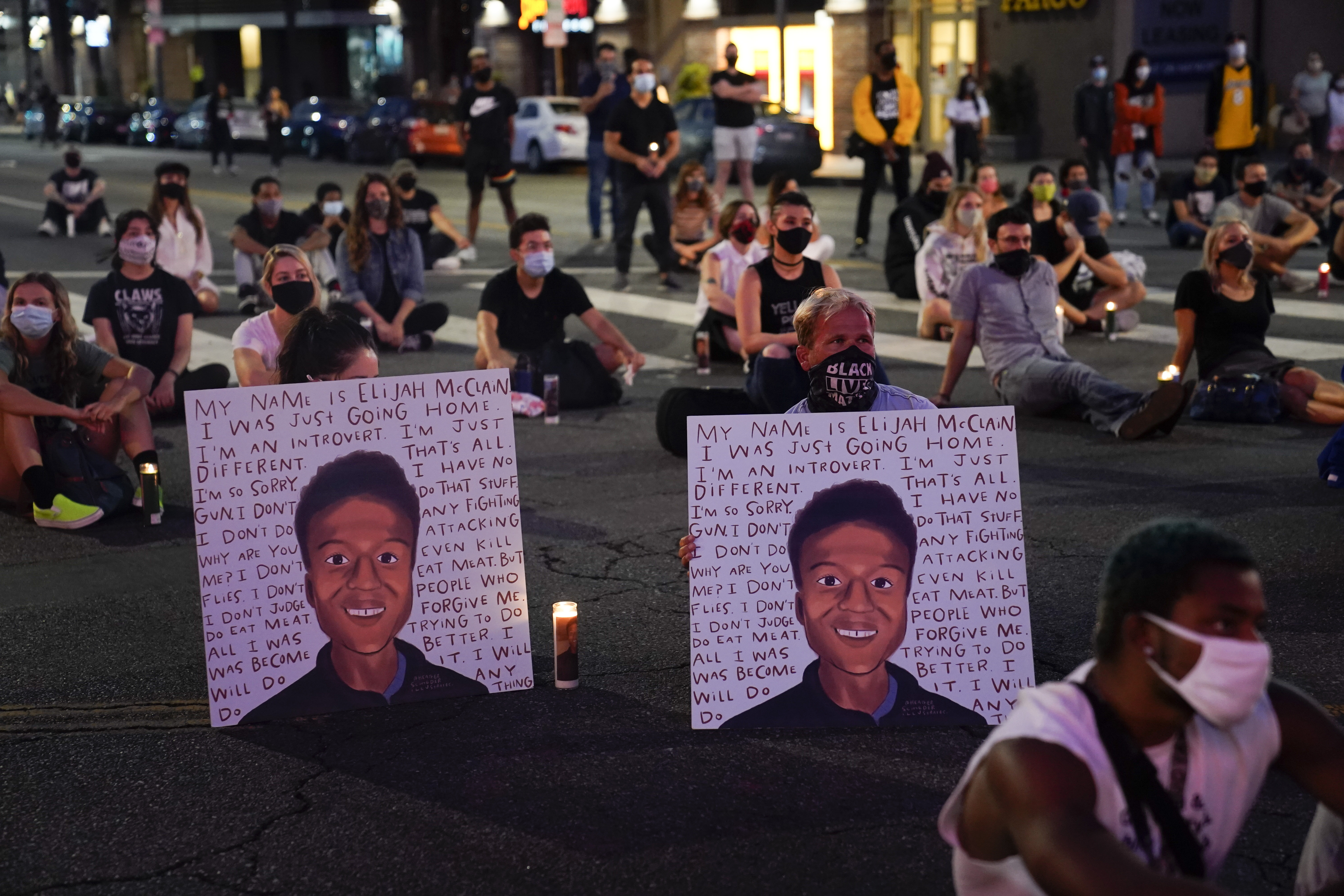 two people hold posters showing images depicting Elijah McClain during a candlelight vigil