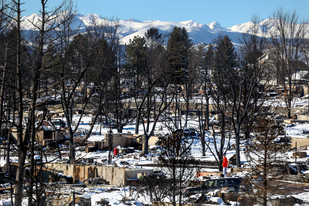 A woman looks at the remains of a home in a neighborhood decimated by the Marshall Fire