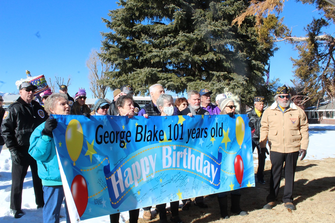 Several people hold a banner saying "happy birthday" to George Blake, who turned 101