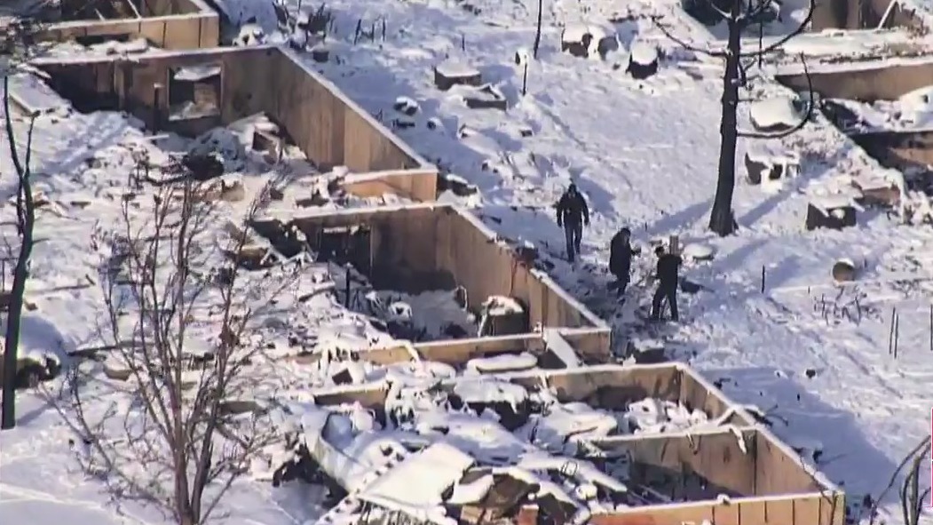 Aerials view of people looking at snow-coated homes that were gutted by fire