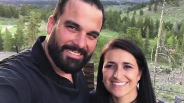 A man and woman smile in front of a vast, forest background