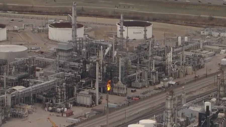 Industrial refinery in daytime with flames emitting from a tall pipe