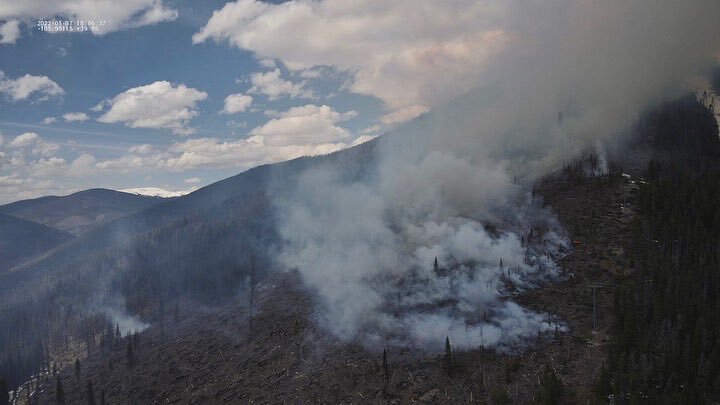 Smoke billows from mountainside in daylight