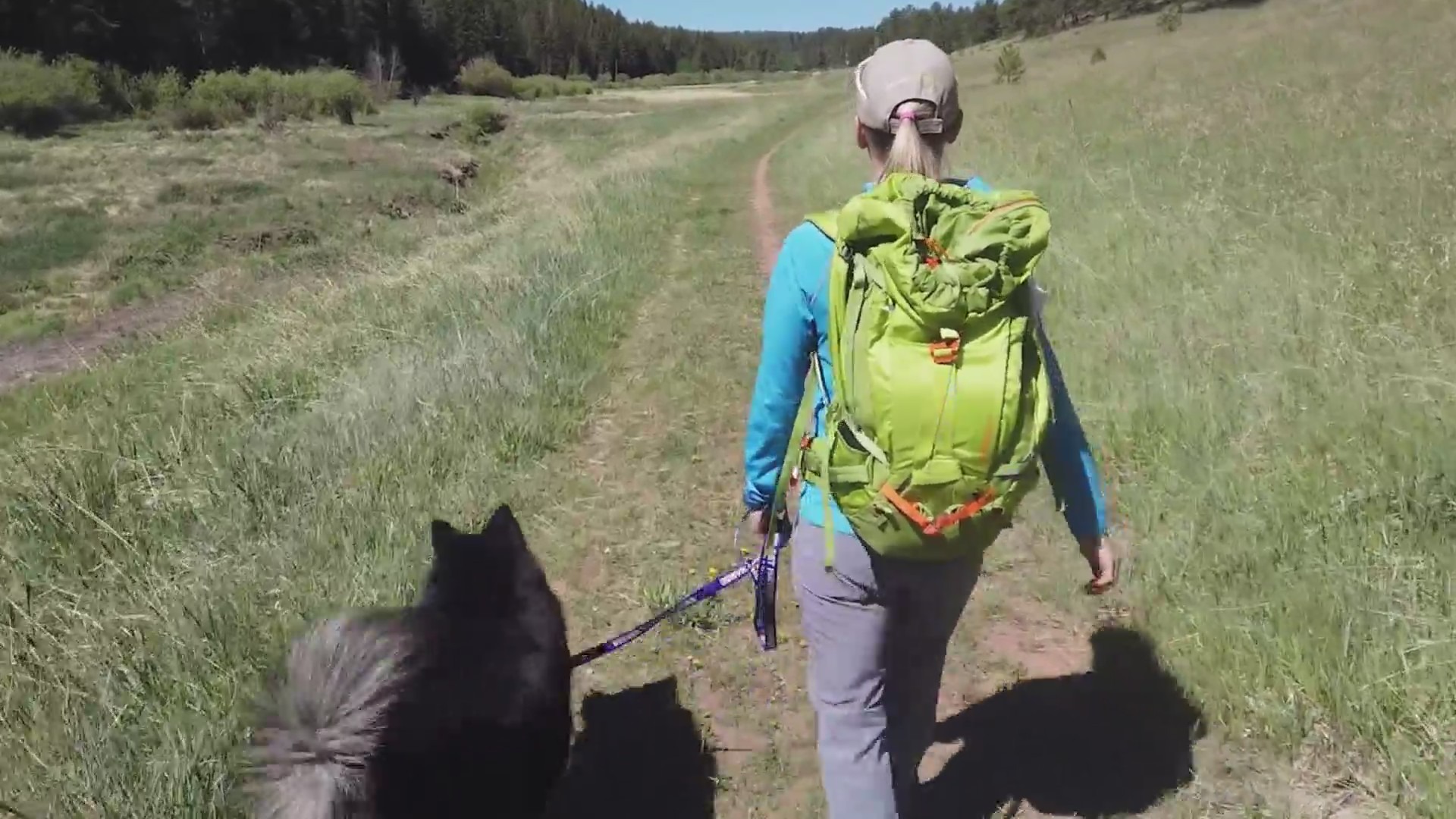 Woman walking ahead on mountain path with black dog on leash