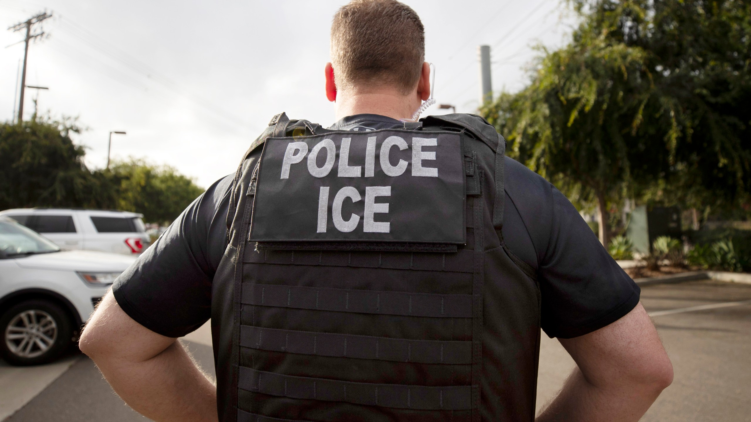 An U.S. Immigration and Customs Enforcement (ICE) officer in a police vest looks on during an operation