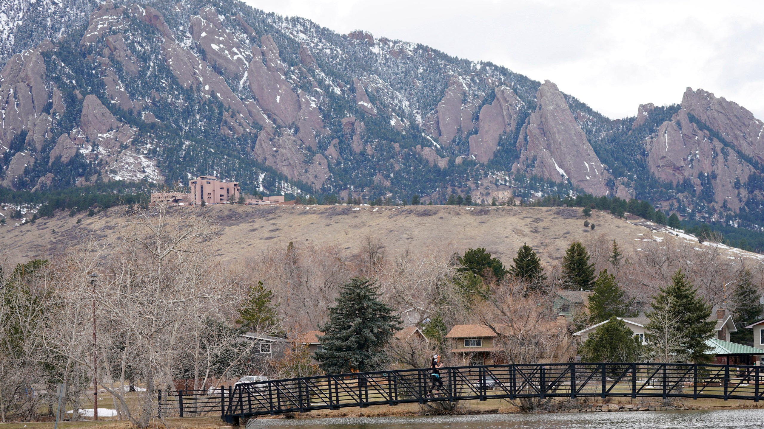 A lone jogger moves across a bridge over the lake in Harlow Platts Community Park with the Flatirons in the background