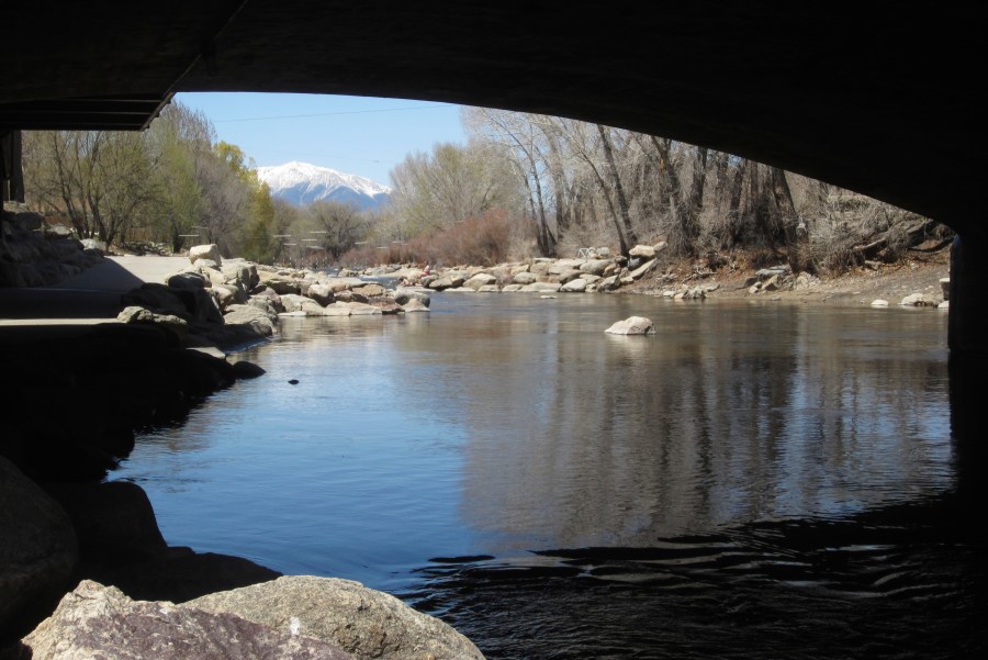 the Arkansas River flows under a bridge in Salida, Colo., with the snow-covered Sawatch Range mountains in the background