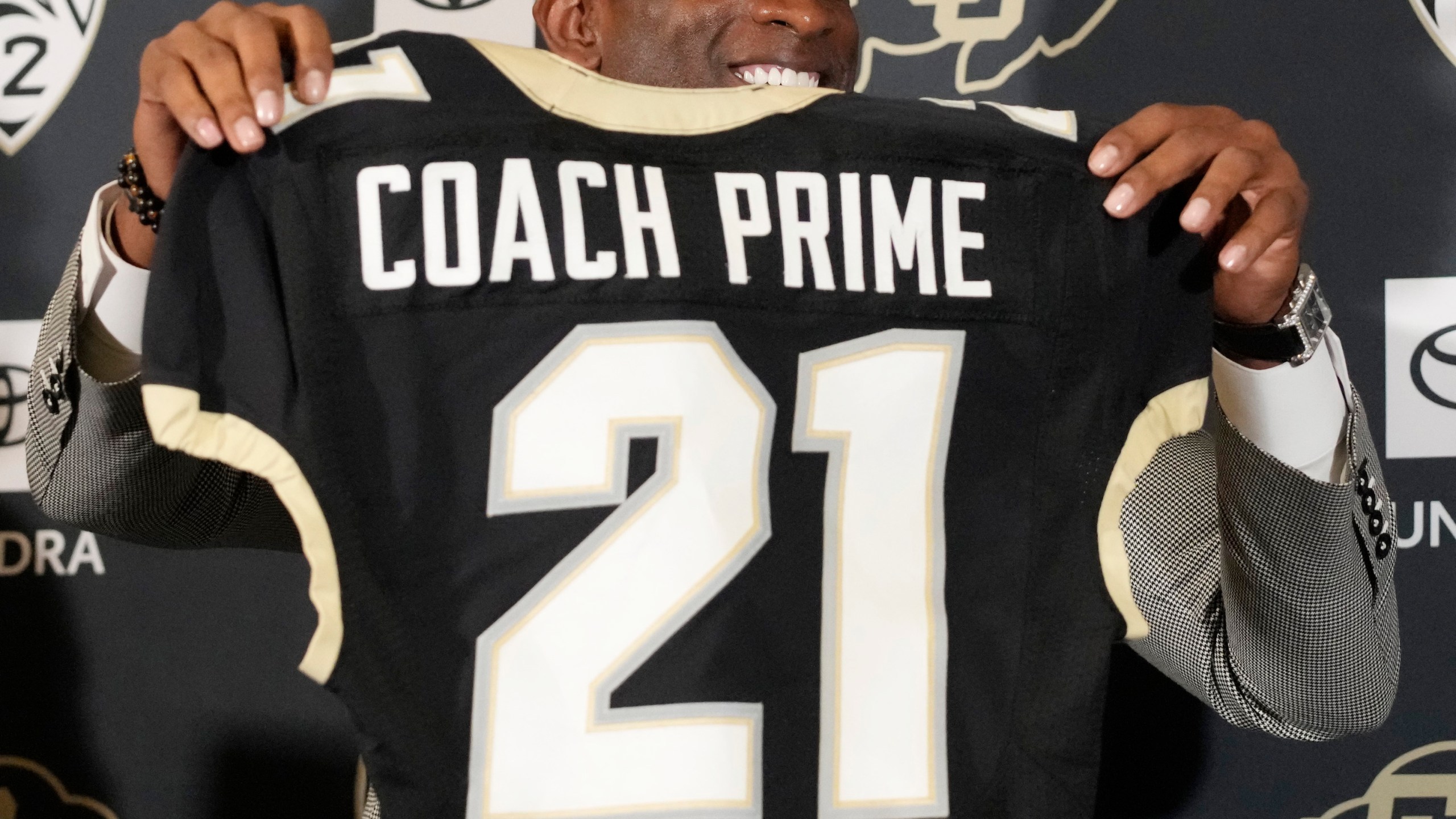 Deion Sanders holds up a jersey before speaking during a news conference