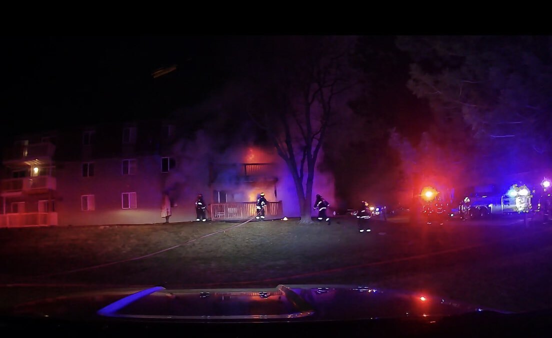 Firefighters in gear with a hose in front of a burning apartment building at night