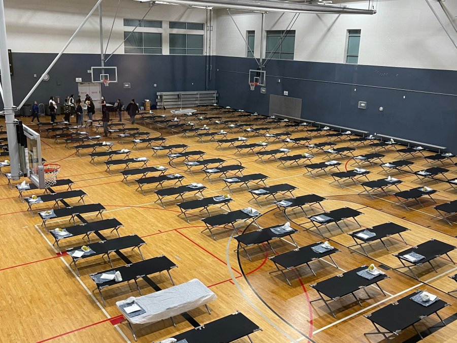 Rows of dozens of cots line an indoor gymnasium