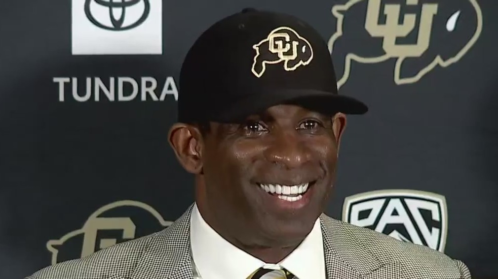 Deion Sanders in a CU Buffs cap and suit at a press conference