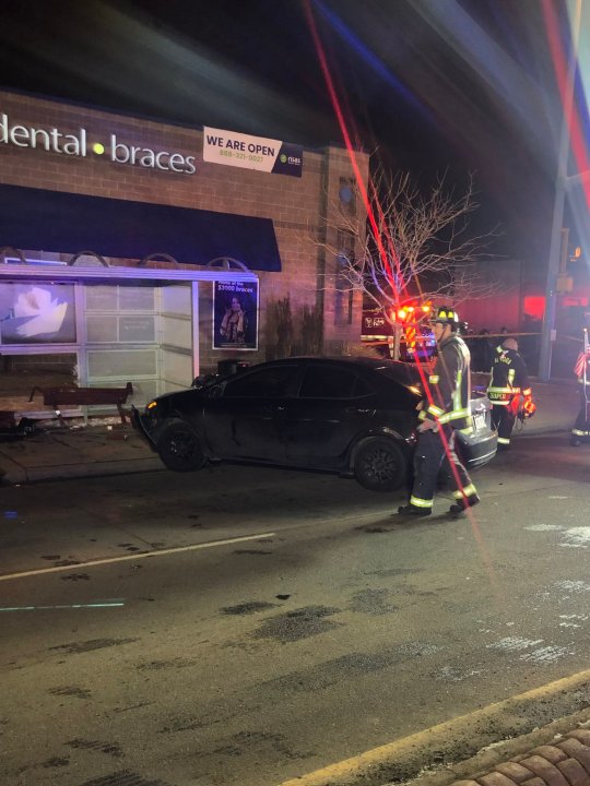 Crashed black sedan next to a bus stop shelter at night