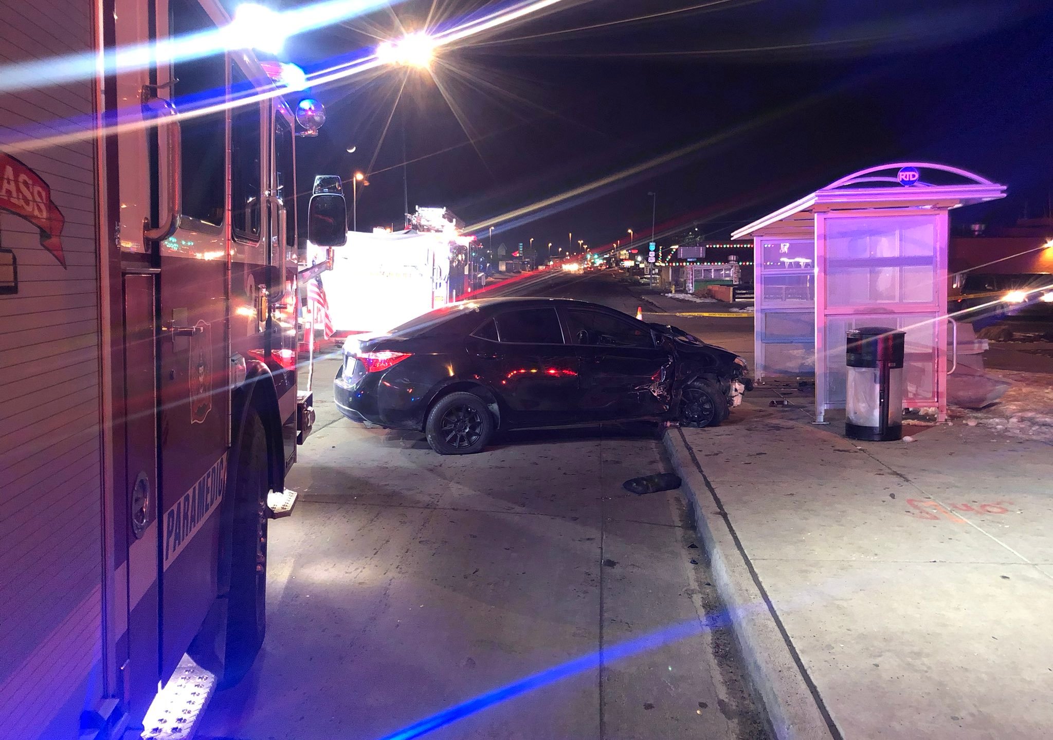 Crashed black sedan next to a bus stop shelter at night