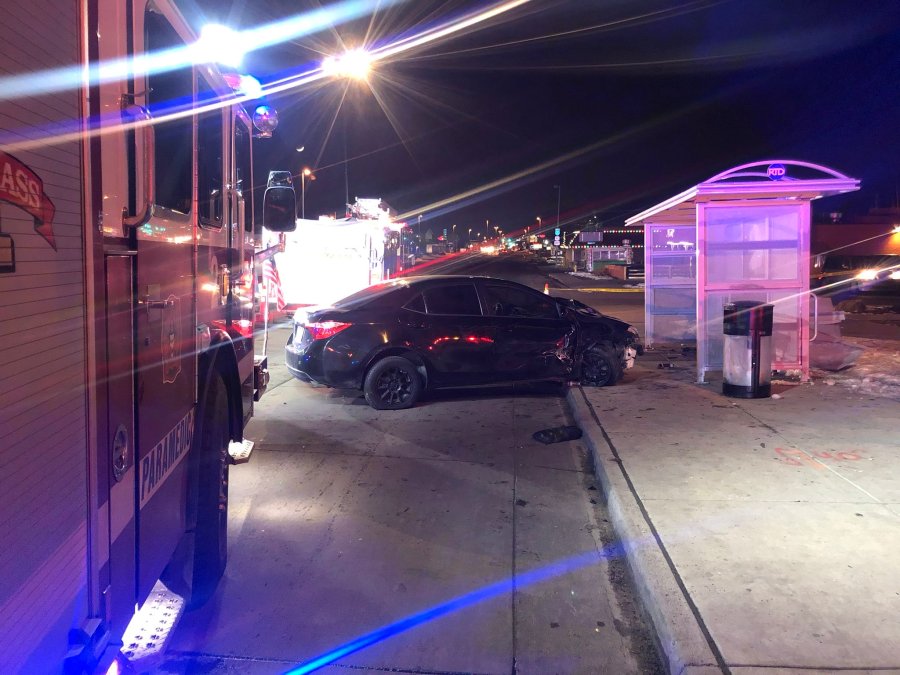 Crashed black sedan next to a bus stop shelter at night