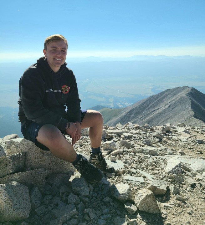 Nick Feinstein, a young man, perched atop Mount Princeton with horizon stretching in the background