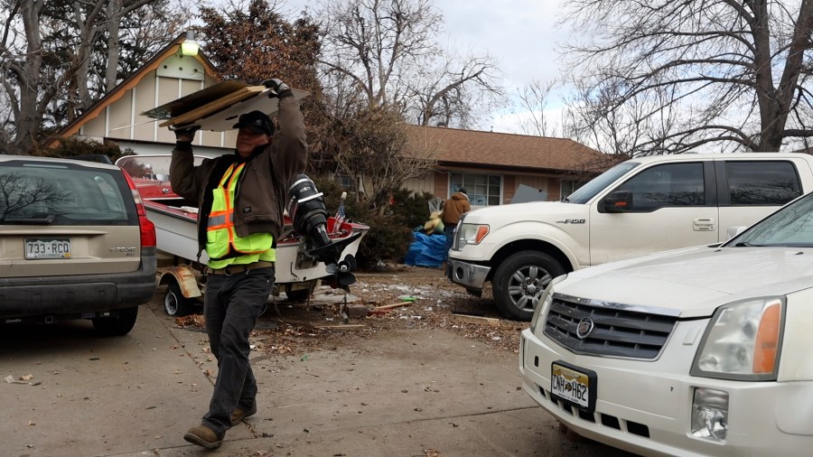 Man in flourescent work vest carries debris out of a home