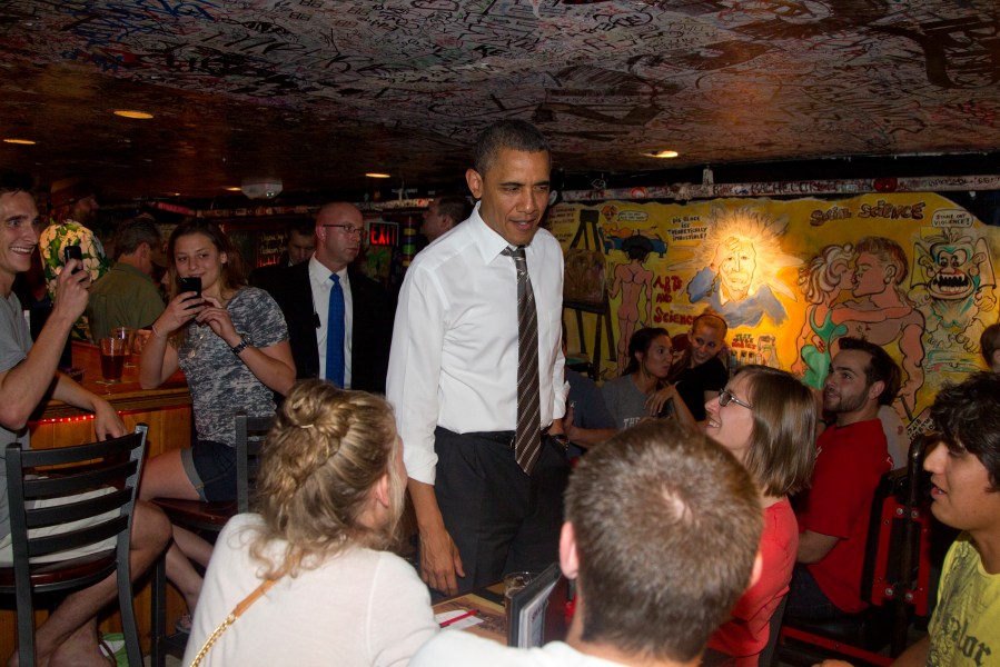 President Barack Obama greets people at The Sink, a small dim interior with art and writing all over the walls and ceiling