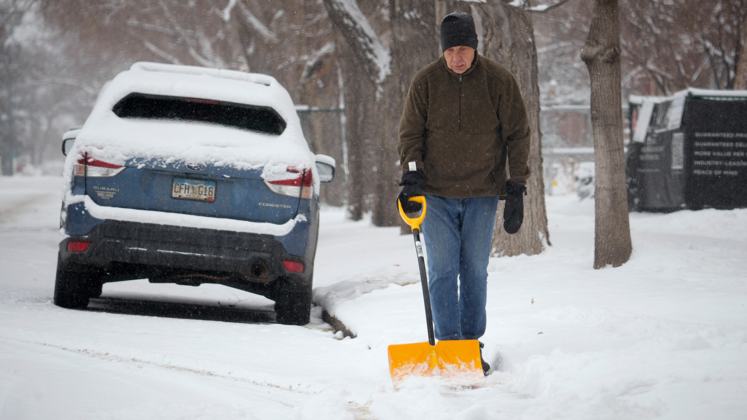 A man uses a shovel to clear snow from a walkway along South Marion Street Parkway