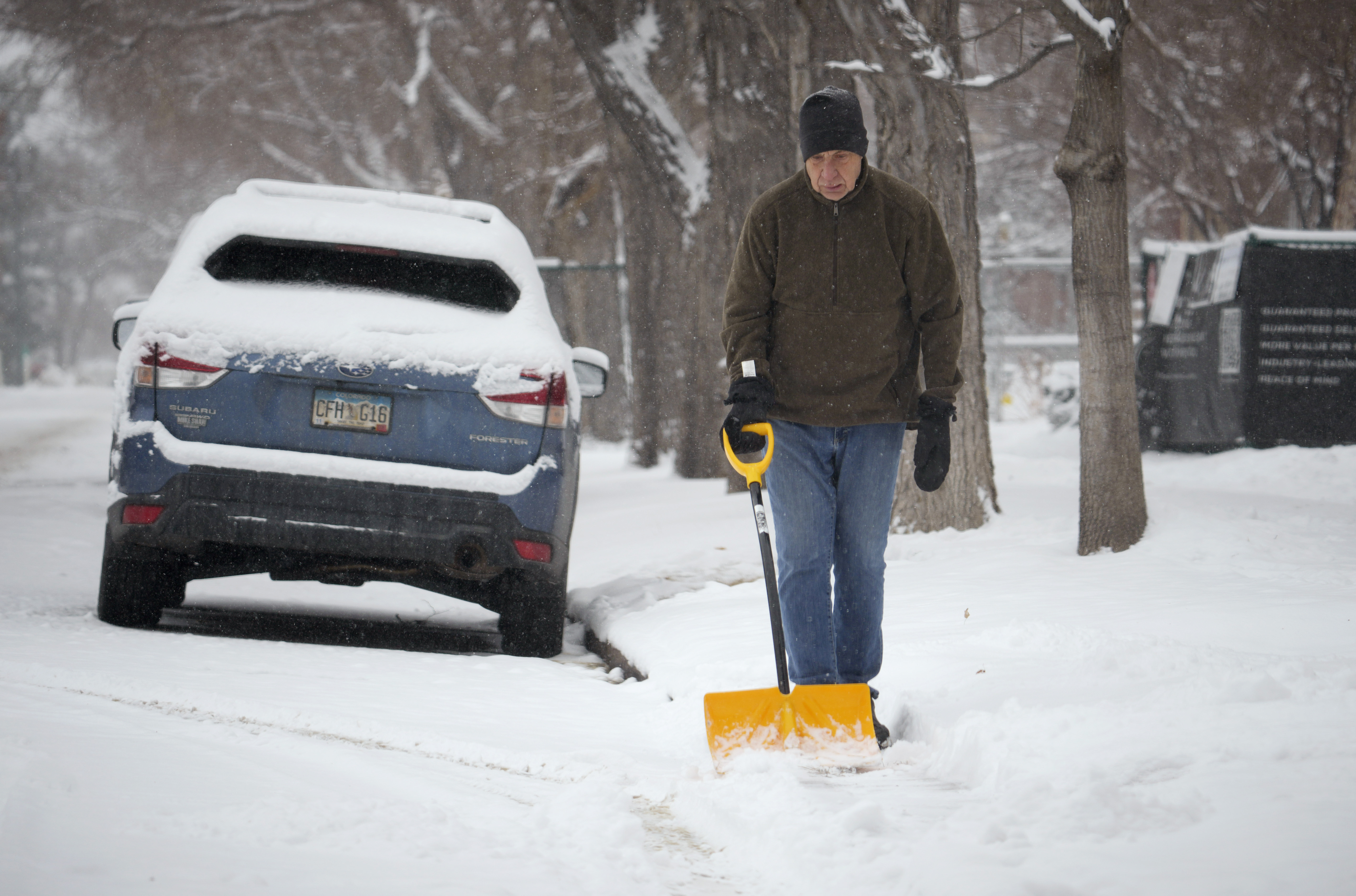 A man uses a shovel to clear snow from a walkway along South Marion Street Parkway