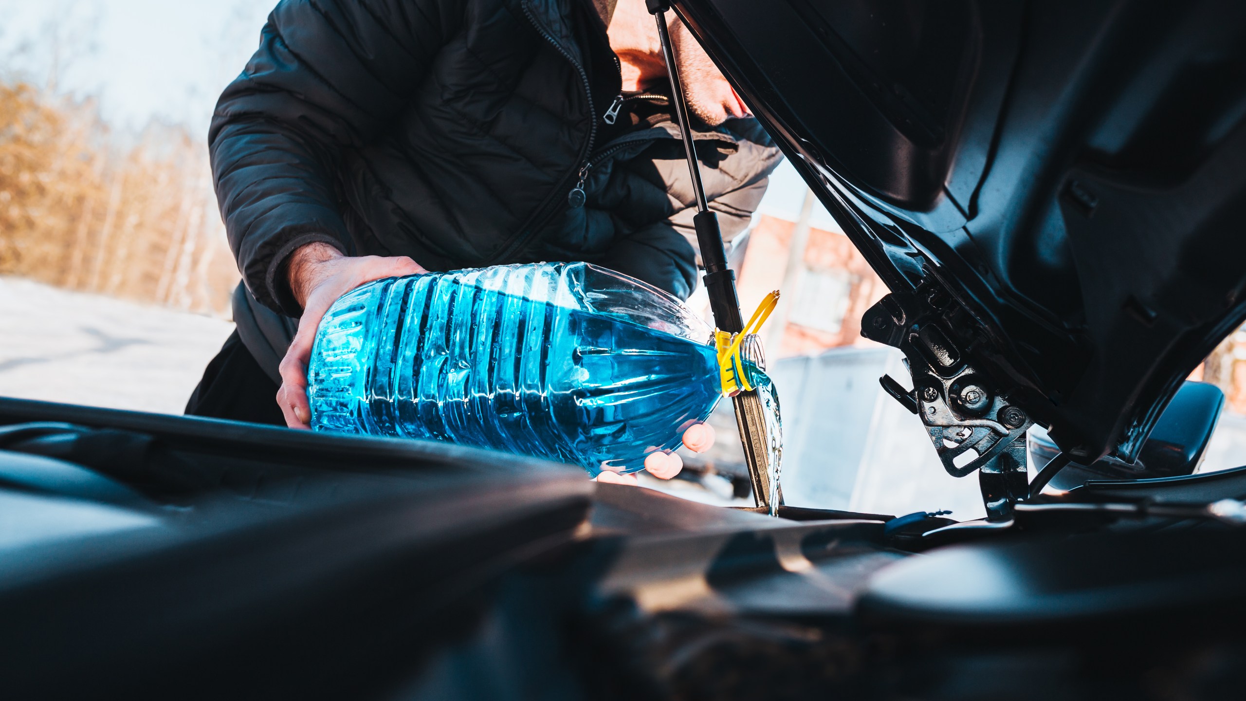 A man pours blue antifreeze liquid from a can into a car washer reservoir