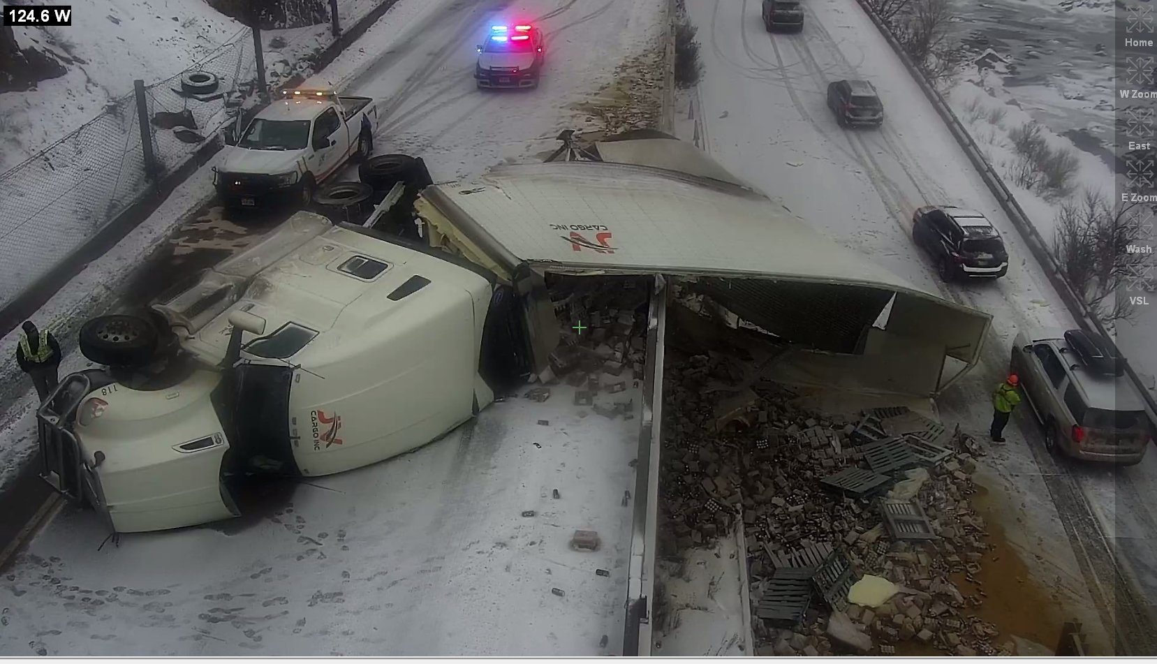 A semi hanging off the side of the highway on its side with cargo spilling out