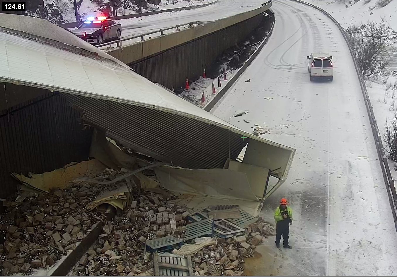 A semi hanging off the side of the highway on its side with cargo spilling out