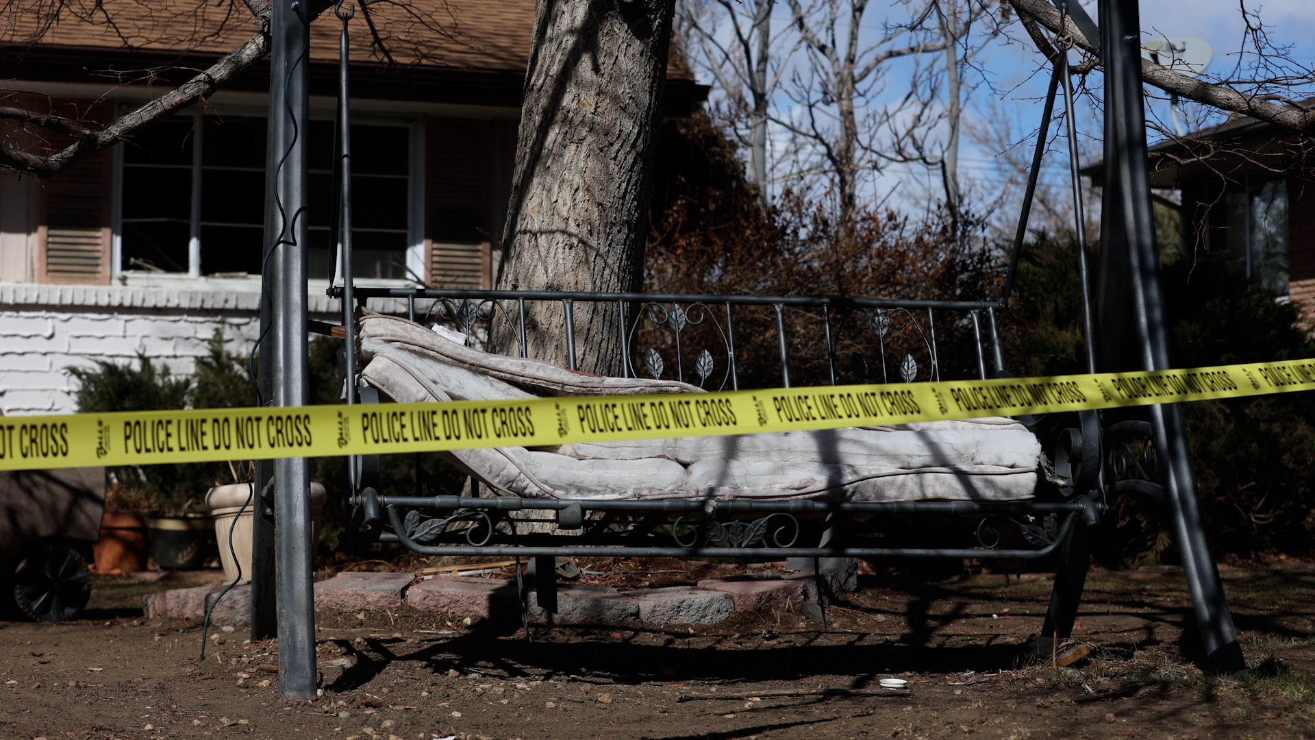 Yellow police tape in front of a swing and refuse in front of a house