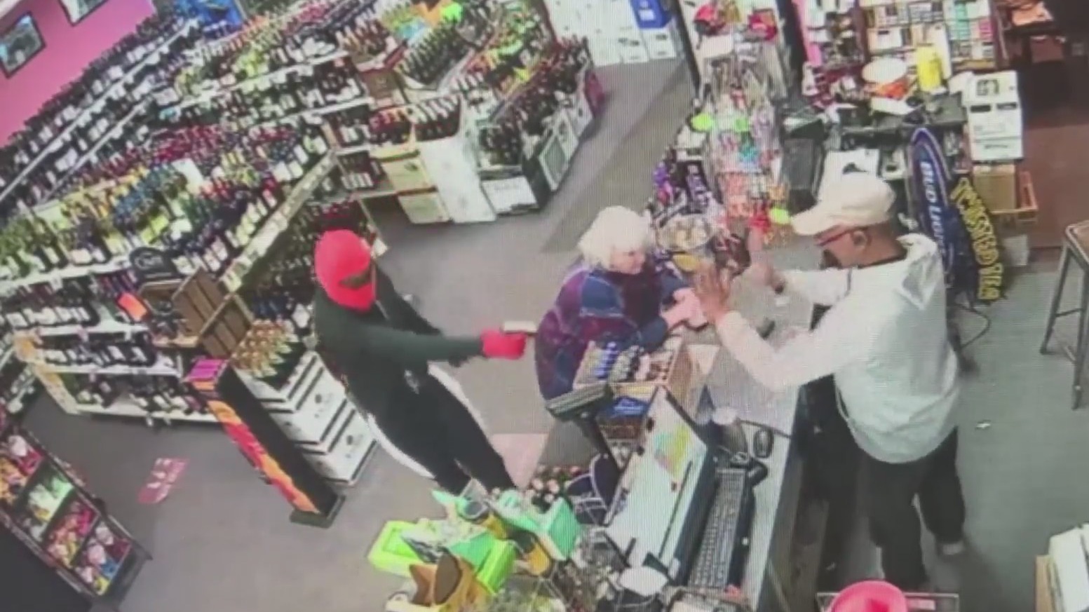 Surveillance video of a robber pointing a gun at a liquor store clerk while a customer stands at the counter next to them