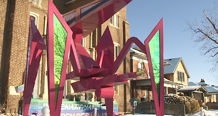 A large, angular sculpture outside a brick building on a residential street