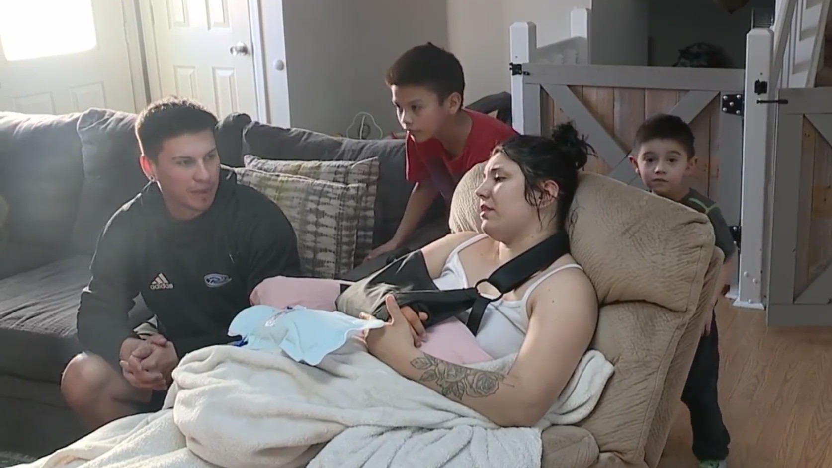 A mother, father and their two boys in a living room, with mother in a sling