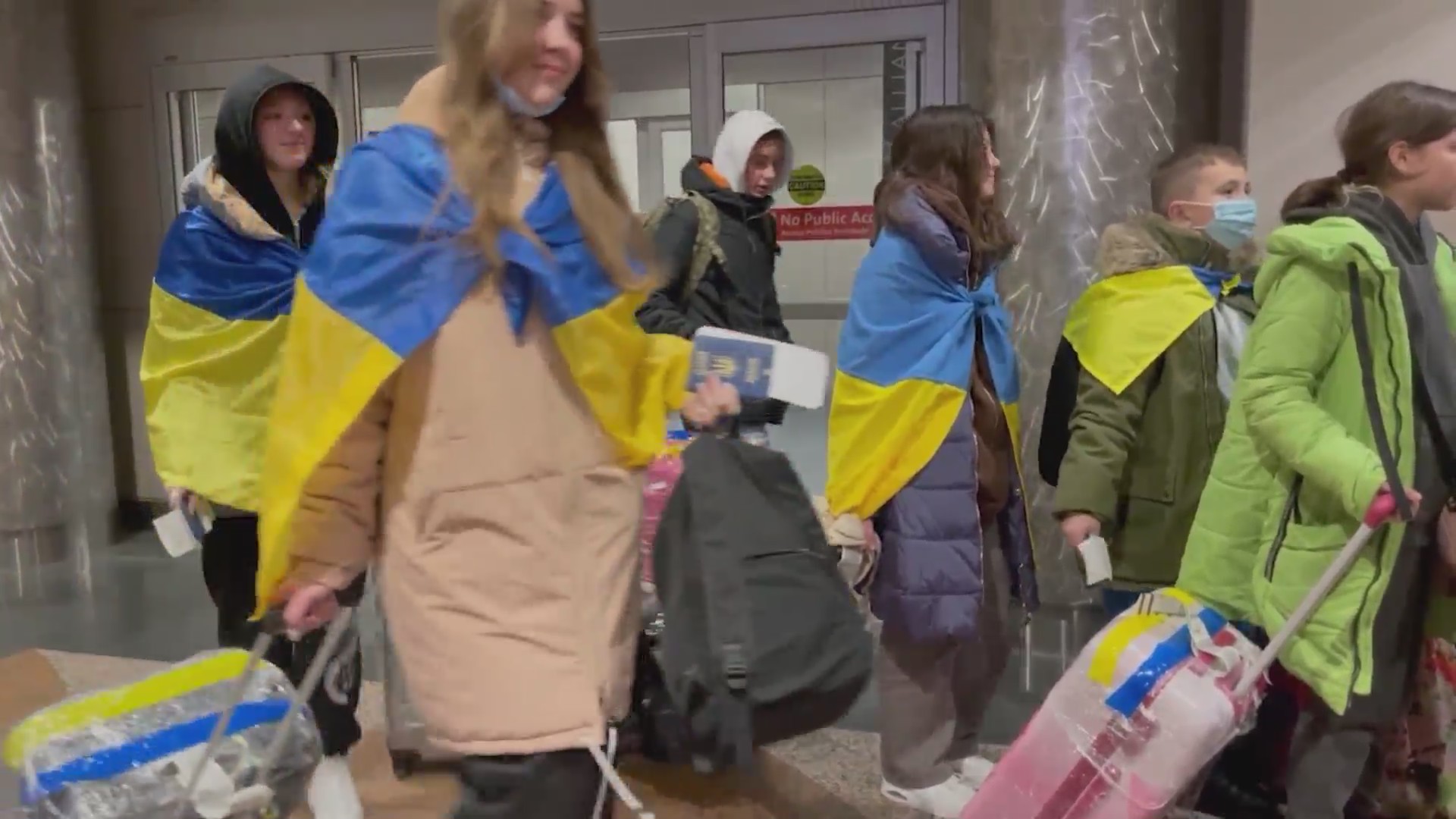 A group of children in Ukrainian flags carrying rolling luggage