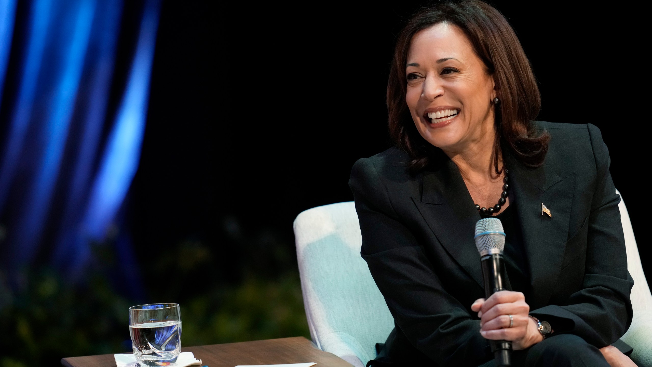 Vice President Kamala Harris smiles while seated and holding a microphone