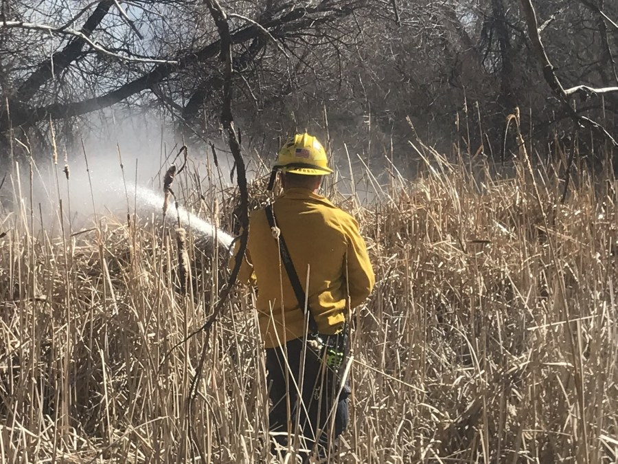 Firefighter using hose on brush fire burning off Parker and Chambers roads in Aurora