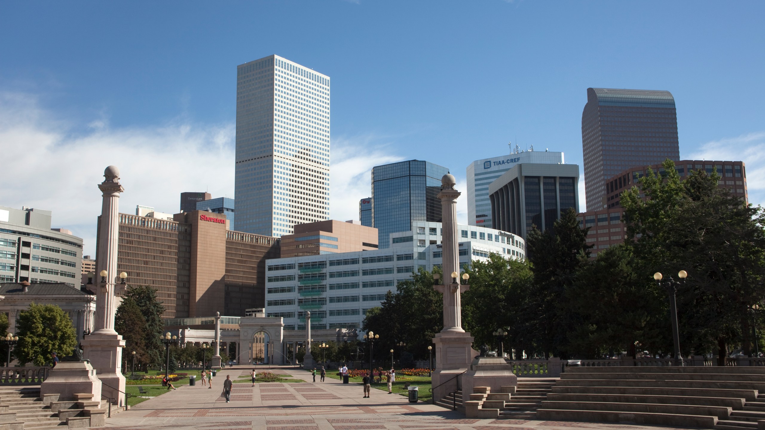 The downtown Denver, Colorado skyline with office buildings, hotels, and apartments rises behind the columns and steps in Civic Center Park