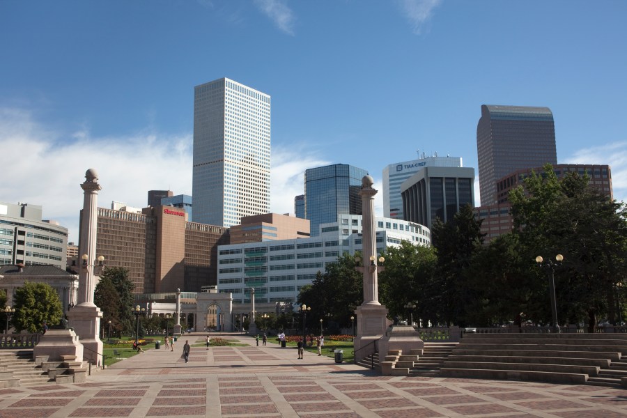 The downtown Denver, Colorado skyline with office buildings, hotels, and apartments rises behind the columns and steps in Civic Center Park