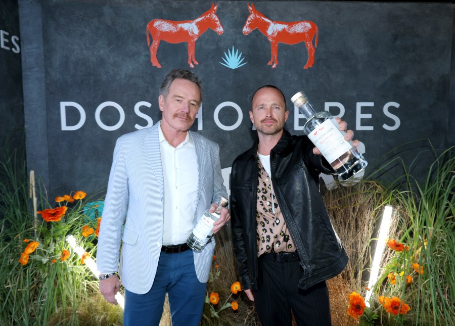 Bryan Cranston and Aaron Paul stand side by side holding bottles of mezcal