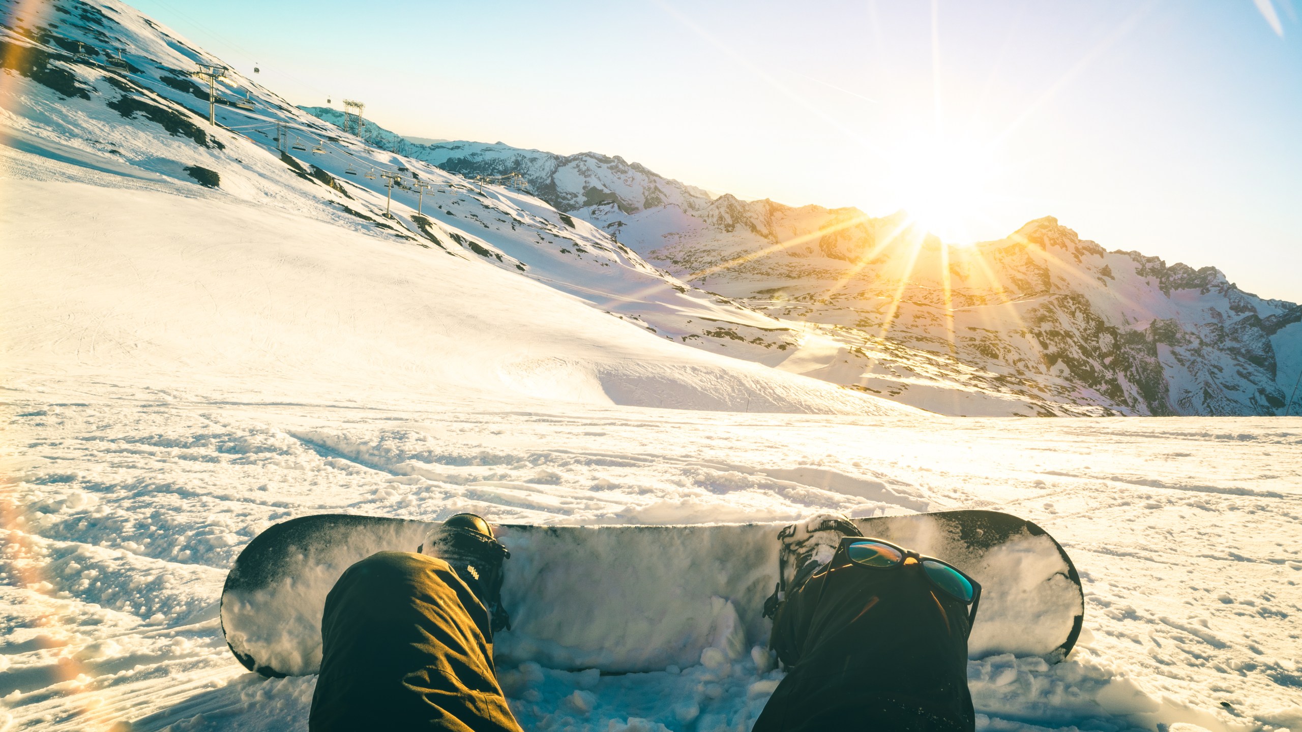 Snowboarder sitting at sunset on relax moment in french alps ski resort - Winter sport concept with adventure guy on top of mountain ready to ride down - Legs view point with teal and orange filter